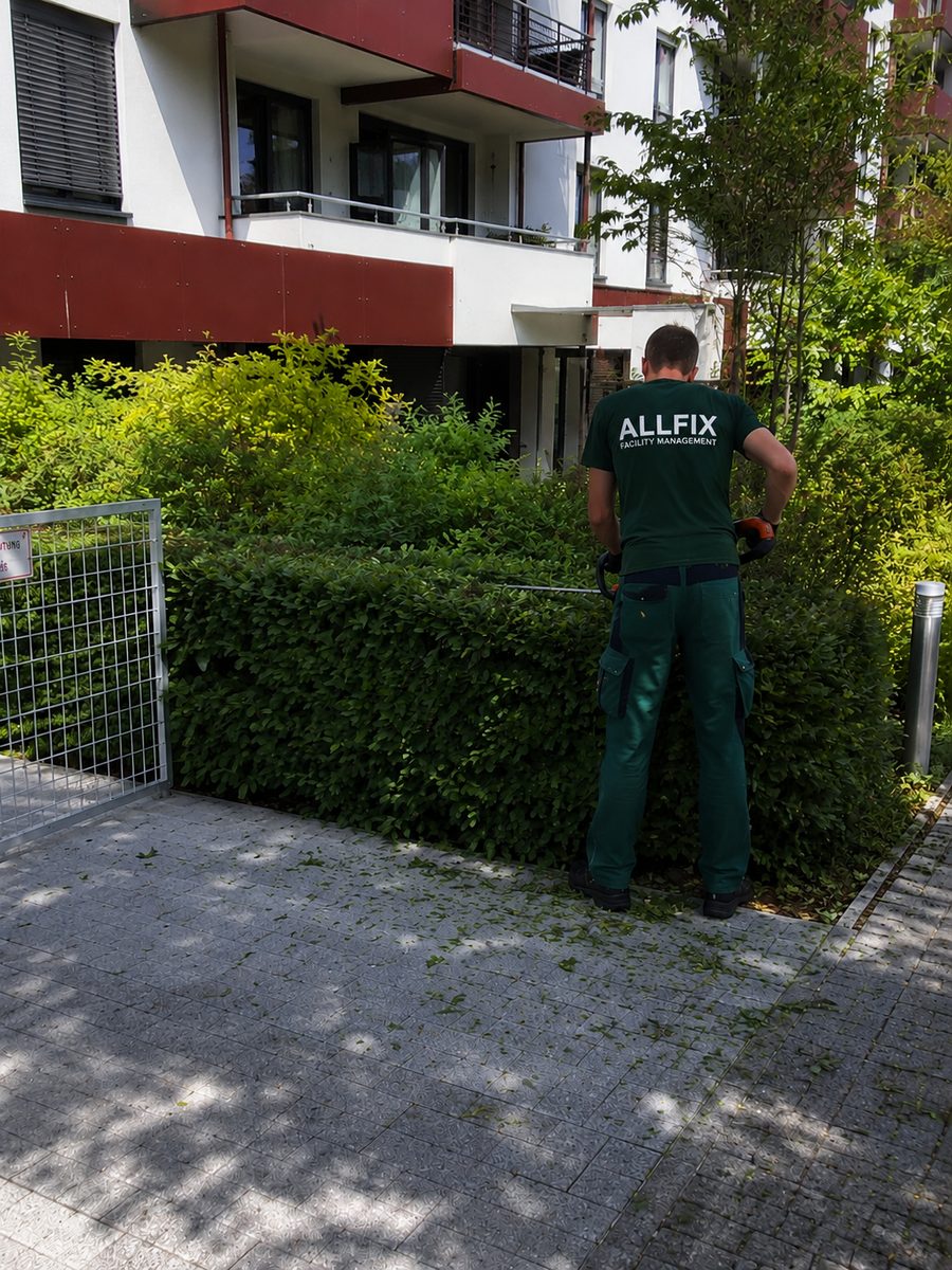 ALLFIX-Mitarbeiter beim Heckenschnitt vor einer Berliner Wohnanlage – Garten- und Grünpflege als Teil des Facility Managements